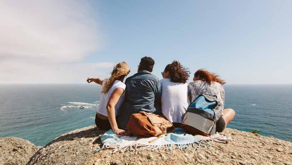 Group of friends on top of hill and enjoying view. Young people sitting on top of a mountain and looking at sea.